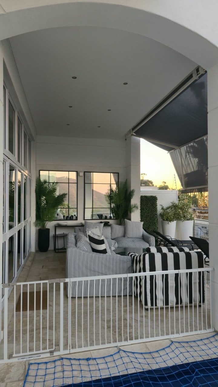 Modern covered patio with striped seating, potted plants, and retractable awning overlooking sunset
