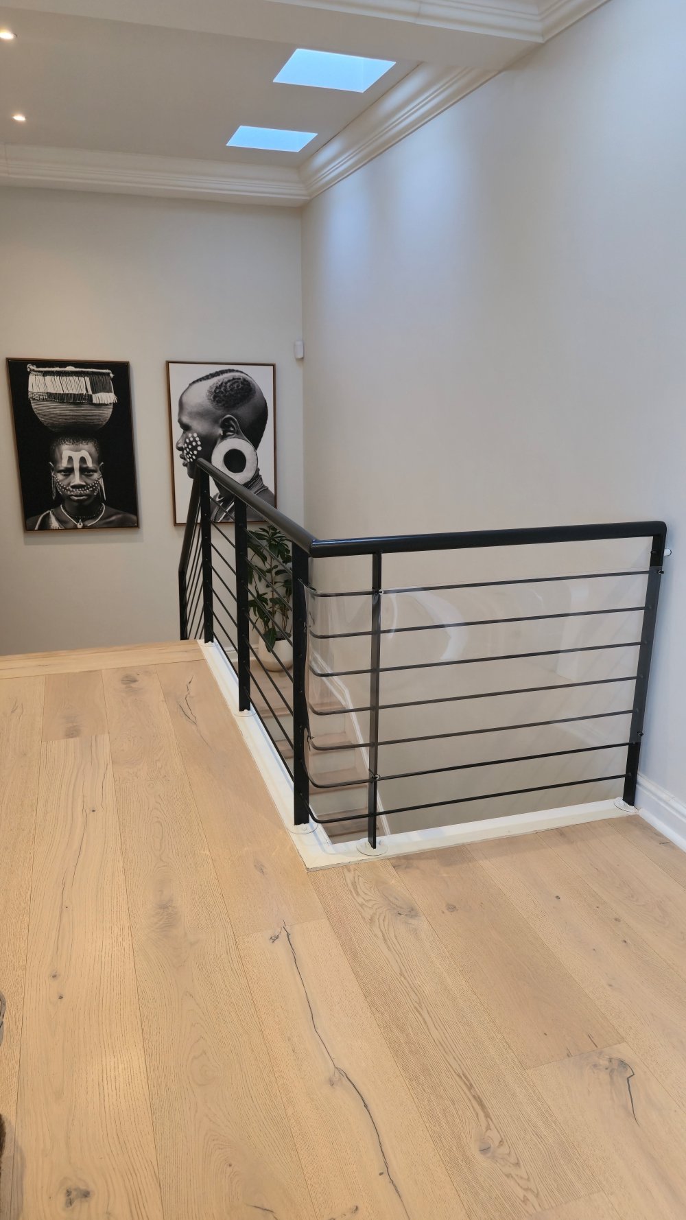 Modern loft space with wooden floor, black metal railing, skylight windows, and two black and white portrait photographs on the wall